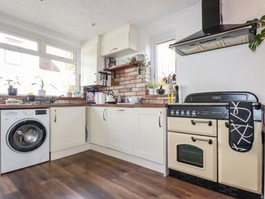 A kitchen with white cabinets a washing machine an oven and plants on the windowsill at Penang in St Austell