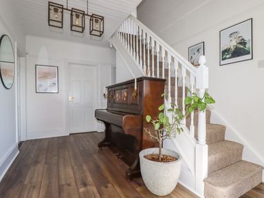 A hallway with a wooden piano a potted plant and carpeted stairs at Penang in St Austell