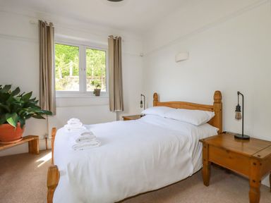 A bedroom with a wooden bed and white bedding with towels on the bed two wooden bedside tables and plants near a window at Penang in St Austell