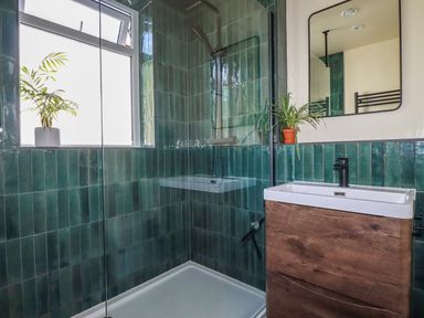 A bathroom with green tiled walls a walk-in shower and a wooden vanity with a sink and mirror at Penang in St Austell