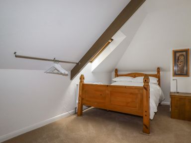 A bedroom with a wooden bed, white bedding, a wooden nightstand, a giraffe picture on the wall, and a metal hanging rail with hangers near a skylight at Penang in St Austell