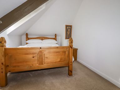 A bedroom with a wooden bed and a bedside table under a slanted ceiling at Penang in St Austell