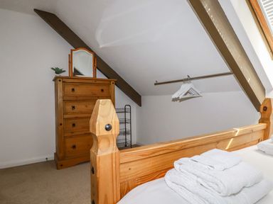 A bedroom with a wooden bed frame a chest of drawers with a mirror folded towels on the bed and hangers on a rail under a sloped ceiling at Penang in St Austell