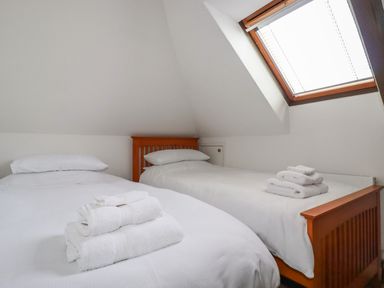A bedroom with two single beds under a slanted ceiling and a skylight window at Penang in St Austell
