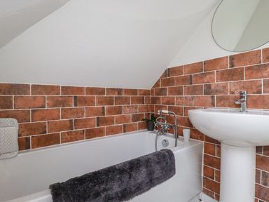 A bathroom with a bathtub and a pedestal sink with brown tiled walls at Penang in St Austell