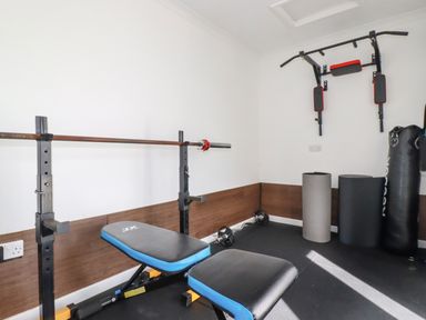 A home gym with a weight bench barbell pull up bar and punching bag at Penang in St Austell