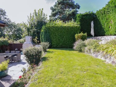 An outdoor garden with a grassy lawn surrounded by bushes and trees and a patio dining set at Penang in St Austell