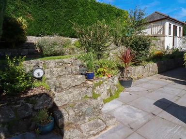 An outdoor stone staircase with potted plants and shrubs near a paved patio and a white house at Penang in St Austell