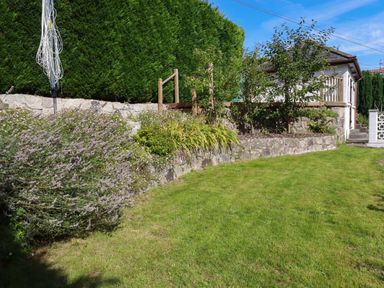 A garden with a green lawn stone retaining walls shrubs and a small house in the background at Penang in St Austell