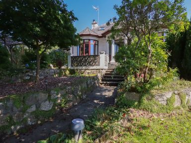 A garden path with steps leading to a house with a bay window and a tiled roof at Penang in St Austell