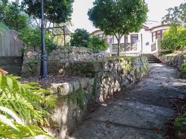 A stone pathway leading to a house with a stone retaining wall and trees at Penang in St Austell