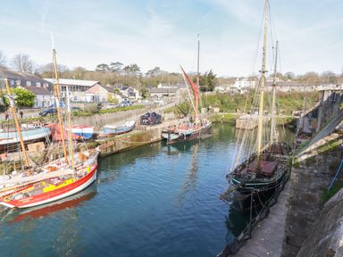 A harbor with several sailboats docked near stone walls and buildings at Penang St Austell