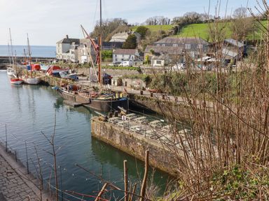 A harbor with boats docked along stone piers and buildings on the hillside at Penang in St Austell