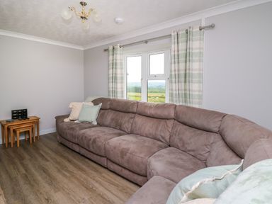 A living room with a large sectional sofa pillows stacked nesting tables and a window with curtains at Ashdale in Bwlch-y-sarnau near Rhayader