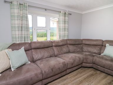 A living room corner with a large brown sectional sofa and green and cream plaid curtains at Ashdale in Bwlch-y-sarnau near Rhayader