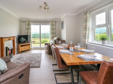 A dining table set with plates and glasses in a room with leather chairs a fireplace a television and sliding glass doors overlooking fields at Ashdale in Bwlch-y-sarnau near Rhayader