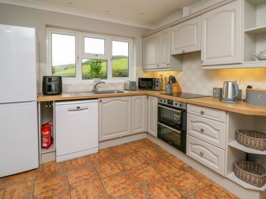 A kitchen with white cabinets wooden countertops a dishwasher oven and window with a view at Ashdale in Bwlch-y-sarnau near Rhayader
