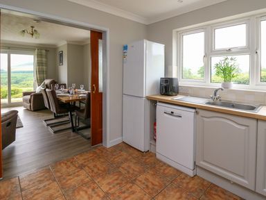A kitchen with a refrigerator dishwasher sink and a dining area visible through an open door at Ashdale in Bwlch-y-sarnau near Rhayader