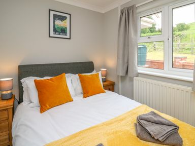 A bedroom with a double bed orange pillows bedside tables lamps and a window at Ashdale in Bwlch-y-sarnau near Rhayader