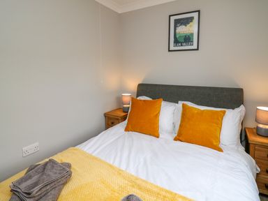 A bedroom with a bed with yellow pillows and a yellow blanket with wooden nightstands and lamps at Ashdale in Bwlch-y-sarnau near Rhayader