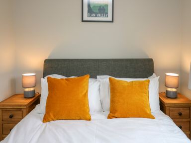A bedroom with a bed with orange pillows and two bedside tables with lamps at Ashdale in Bwlch-y-sarnau near Rhayader