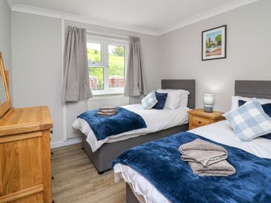 A bedroom with two single beds a wooden dresser a window with curtains and a framed picture on the wall at Ashdale in Bwlch-y-sarnau near Rhayader