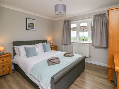 A bedroom with a double bed bedside tables lamps a window with curtains and a wooden wardrobe at Ashdale in Bwlch-y-sarnau near Rhayader