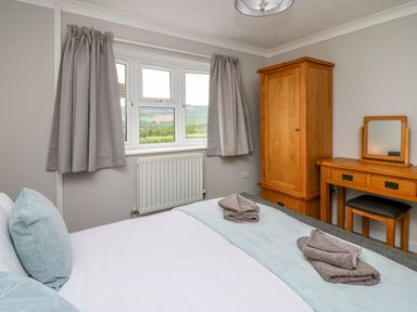 A bedroom with a bed pillows towels on the bed a wooden wardrobe and a dressing table with a stool at Ashdale Bwlch-y-sarnau near Rhayader