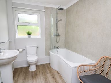 A bathroom with a bathtub shower toilet sink a wicker chair and a small plant on the window sill at Ashdale in Bwlch-y-sarnau near Rhayader