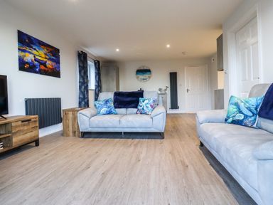 A living room with two sofas and colorful pillows a wooden cabinet and paintings at 2A The Anchorage in Beadnell