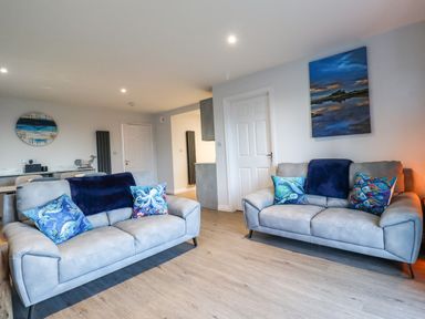 A living room with two grey sofas with blue cushions and a painting on the wall at 2A The Anchorage in Beadnell