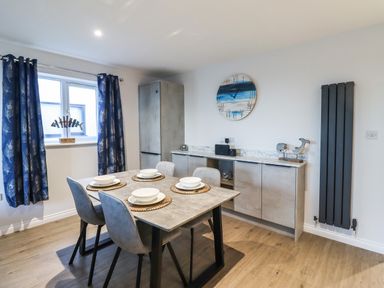 A dining room with a table set for four and a sideboard with a clock on the wall at 2A The Anchorage in Beadnell