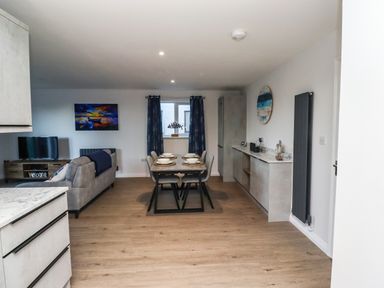 An open plan living room and dining area with a dining table set for four and a sofa with a TV at 2A The Anchorage in Beadnell