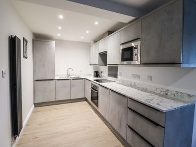 A kitchen with grey cabinets a marble countertop a built in oven microwave and sink at 2A The Anchorage in Beadnell