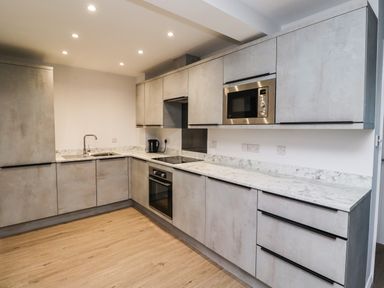 A kitchen with grey cabinets white marble countertops built in microwave oven and electric stove at 2A The Anchorage in Beadnell