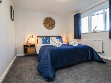 A bedroom with a double bed covered in a blue quilt and white rolled towels on top at 2A The Anchorage in Beadnell
