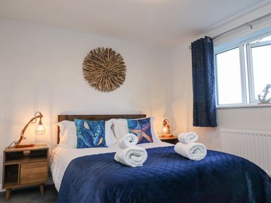 A bedroom with a bed with rolled towels and blue bedding at 2A The Anchorage in Beadnell