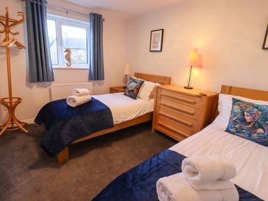 A bedroom with two single beds with blue bed runners and towels on top a wooden chest of drawers and coat rack at 2A The Anchorage in Beadnell