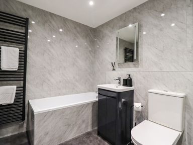 A bathroom with a bathtub sink with vanity mirror toilet and black towel rack at 2A The Anchorage in Beadnell