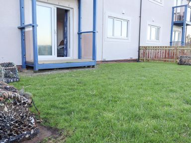 A grassy yard with a small wooden deck outside sliding glass doors on a ground floor apartment at 2A The Anchorage in Beadnell