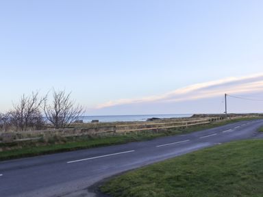 A road with grassy area and a wooden fence overlooking the sea at 2A The Anchorage in Beadnell
