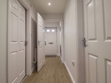 A hallway with multiple white doors and wood flooring at 2A The Anchorage in Beadnell