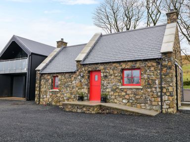 A stone cottage with red door and windows beside a black modern building at The Croft in Newtown-Crommelin near Cloughmills