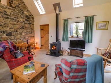 A living room with stone wall a wood stove and checkered armchairs at The Croft in Newtown-Crommelin near Cloughmills