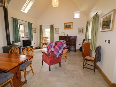 A living room with a piano armchair dining table and wood stove at The Croft in Newtown-Crommelin near Cloughmills