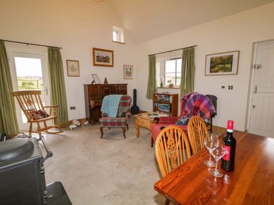 A living room with chairs a piano a small bookshelf and a table with wine glasses and a bottle at The Croft in Newtown-Crommelin near Cloughmills