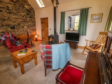 A living room with a stone wall wood stove wooden chairs television and a piano at The Croft in Newtown-Crommelin near Cloughmills