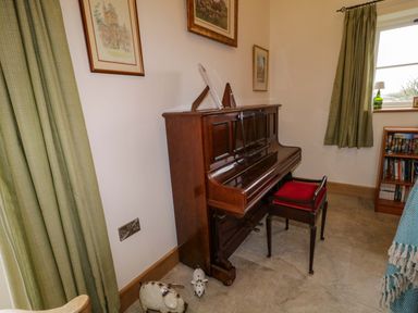 A room with an upright piano and a piano bench with a red cushion near a window with green curtains at The Croft in Newtown-Crommelin near Cloughmills