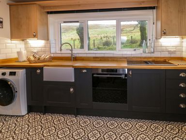 A kitchen with wooden countertops black cabinets a washing machine a sink an oven and patterned floor tiles at The Croft in Newtown-Crommelin near Cloughmills