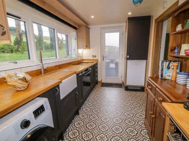 A kitchen with patterned floor tiles a wooden countertop black cabinets a washing machine a white sink and a door leading outside at The Croft in Newtown-Crommelin near Cloughmills
